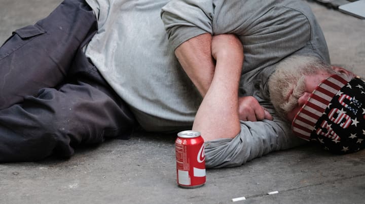 man lying on sidewalk with beer can