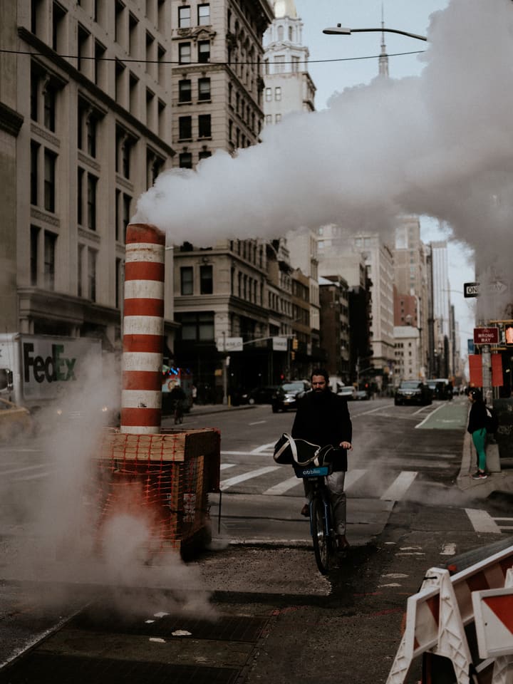 cyclist passing steam stack in city